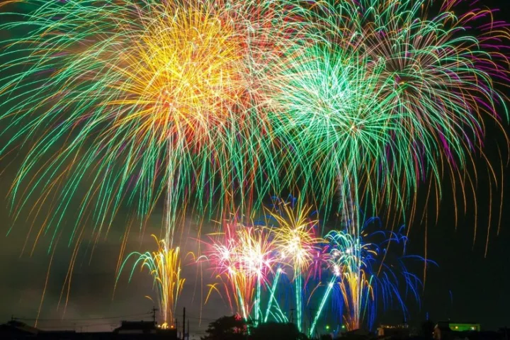 Vibrant fireworks display with multi-colored bursts against a dark night sky over a silhouetted cityscape.